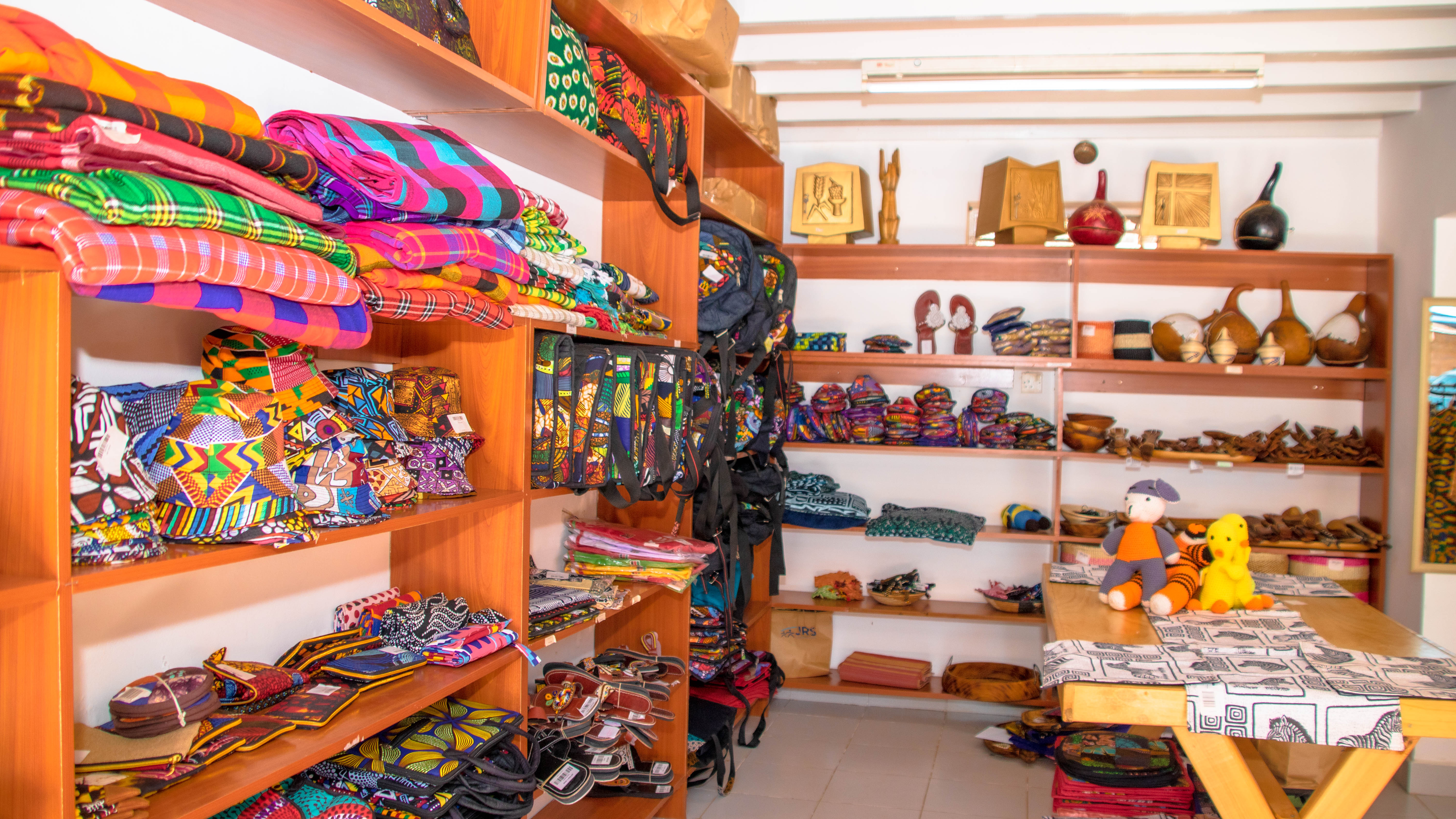 Shop shelves with colorful folded Maasai shuka fabrics, bags, and various crafts